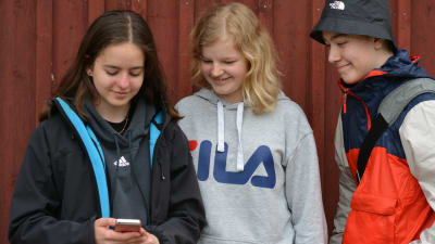 Tre skolelever som tittar på en mobiltelefon.