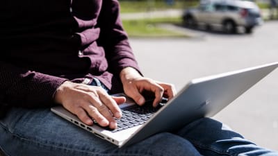En person använder en laptop utomhus.
