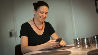 En kvinna sitter med en telefon vid ett bord.