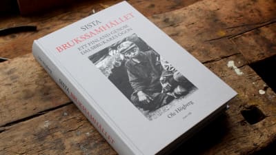 Ole högbergs bok Sista brukssamhället ligger på en brun hyvelbänk. En svartvit bild på en smutsig pojke i basker på omslaget.