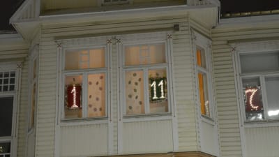 Ett hus med flera upplysta nummer i fönstren som en fönsterjulkalender.