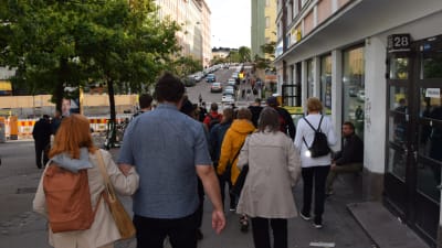 En grupp människor går nerför en gata i Sörnäs, deltar i en guidad rundtur som leds av Pertti Stenman.