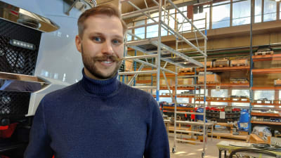 En man i blå tröja står i en hall där det tillverkas lastbilar, han heter Akseli Mylläri.