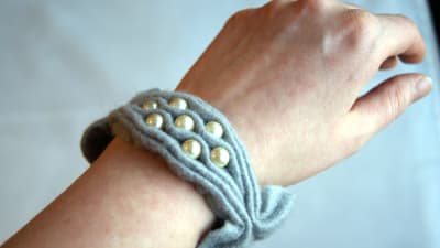 Ett armband av rynkat grått filttyg med pärlbroderi som är knutet runt en handled.