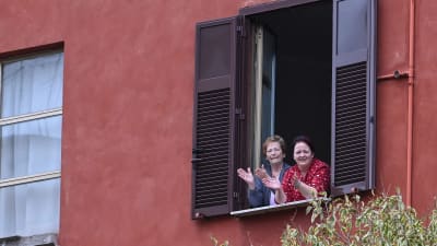 Två kvinnor vinkar och klappar i händerna. Här under devisen "En applåd för Italien"  ( "Un applauso per l'Italia") i distriktet Garbatella i Rom 14.3.2020. 