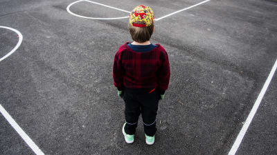 En pojke står på en asfalterad plan med ryggen mot kameran.