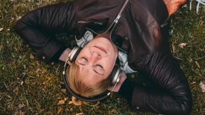 Nainen kuuntelee kuulokkeista musiikkia nurmikolla.