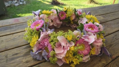 En blomsterkrans av gul allium, rosa hortensia, daggkåpa, lila klematis och rosa krysantemum.