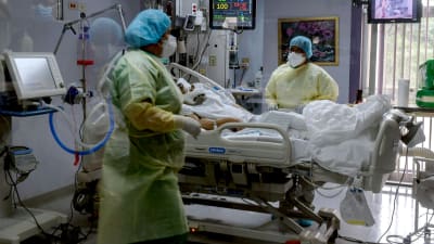 Vårdare i skyddsutrustning står vid en patients säng.