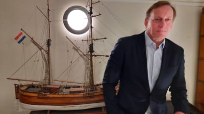 A man in a suit stands next to a model ship