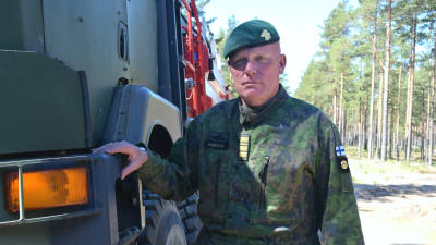 En bild på en man i militärkläder. Han har en grön barett och står lutad mot en lastbil.