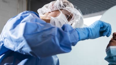 Sjukskötare i skyddsutrustning tar coronaprov på patient.