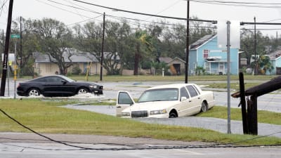 En mörk bil kör förbi en vit bil som ligger i översvämningsvatten i Rockport, Texas den 26 augusti 2017 efetr orkanen Harvey.