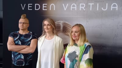 Ilja Rautsi, Emmi Itäranta och Saara Saarela poserar framför en stor filmplansch av Veden vartija.