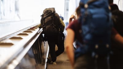 Resenärer med stora ryggsäckar står i en rulltrappa på Helsingfors-Vanda flygfält.