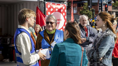 Valkampanj på Sergels torg i Stockholm: två kvinnor talar med två personer i blå partivästar medan en äldre man ser på en bit ifrån.