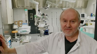 Sakari Orava står i dörröppningen till en operationssal i vit läkarrock. 