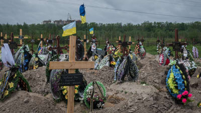 Nygrävda gravar på rad. Vid gravarna finns kors i trä och blommor. Ukrainas flagga vajar på flera ställen.