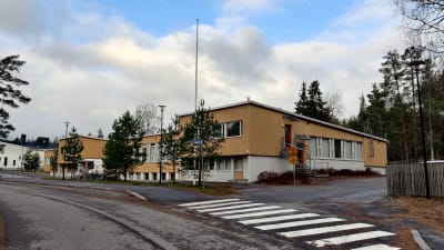 En gulgrå byggnad bakom några tallar som är Merituulen koulu i Ingå.
