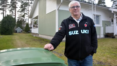 En man som står vid ett avfallskärl, i bakgrunden ett småhus.