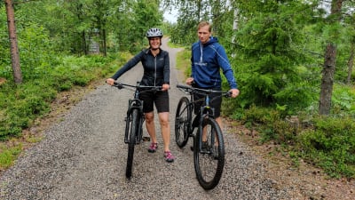 En man och en kvinna står bredvid var sin terrängcykel på en sandväg.