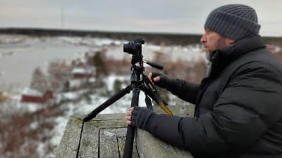 En man med vinterkläder står uppe i ett torn och fotograferar landskap