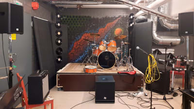En träningslokal med en liten scen och instrument så som trummor.