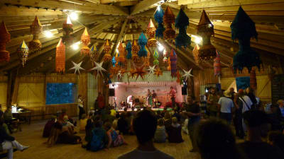 Konsert på dansplatsen i Gumnäs i Pojo, inomhus, farggranna lyktor hänger i taket., liten publik sitter på golvet, en del står, en liten orkester spelar längst framme.