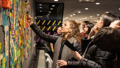 People looking at and taking pictures of a puzzle that is hanging on the wall.