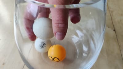 Tre pingisbollar i en glasburk, en hand lyfter upp en av bollarna.