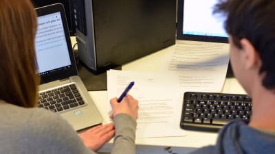 En kvinna sitter med penna och papper och försöker lära en kille att skriva CV.