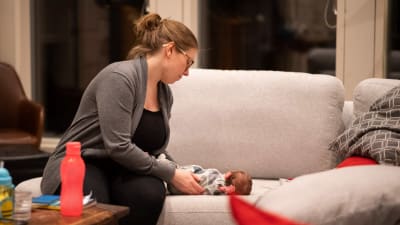 Kvinna pysslar om liten baby på soffa.