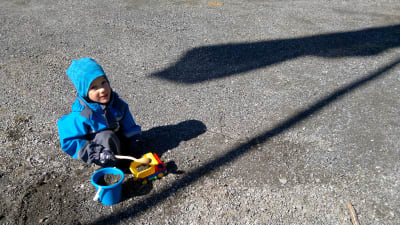 Fyraårig pojke leker med hink och lastbil i gruset.