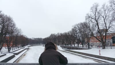 En person i vinterrock står vid Domkyrkobron och tittar ner i Aura å.