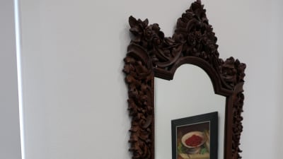 En tavla speglar sig i en gammal spegel med snickrad träram