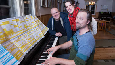 Tre personer vid ett piano
