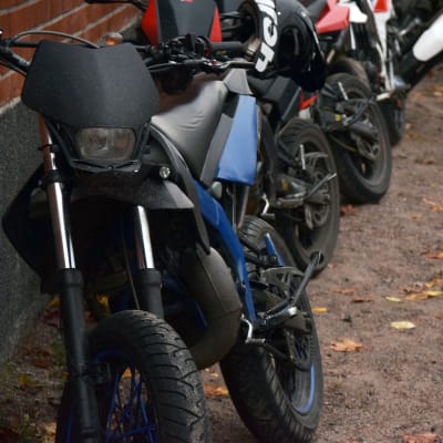 En moped står lutad mot en vägg. I bakgrunden syns fler mopeder.