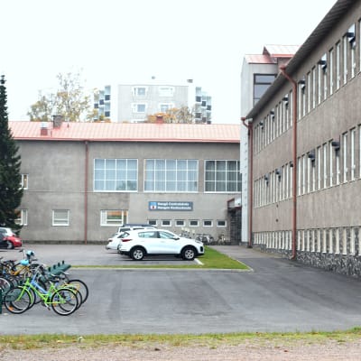 Grå skolbyggnad med parkeringsplats utanför.