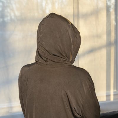 Anonyymi sähköyliherkkä säteilyltä suojaava huppari päällään seisoo ikkunan edessä, ikkunassa säteilyltä suojaavat verhot