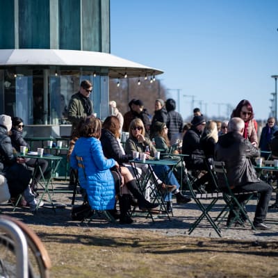 Ihmisiä Cafe Kompassin terassilla Kaivopuiston rannassa kevätpäiväntasauksena.
