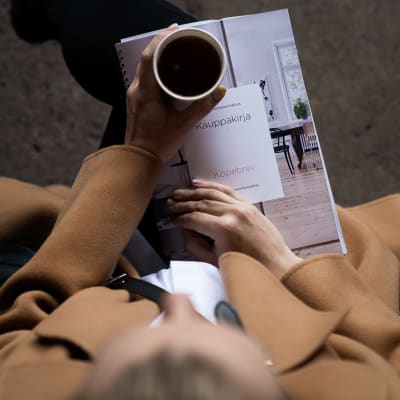 En kvinna sitter med ett köpebrev och en kaffe i famnen.
