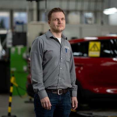 Verkstadschef Sebastian Wallén i verkstadshallen vid Borgå Autosalpa, bakom honom en röd Volvo elbil. 