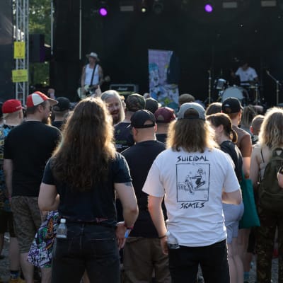 Festivaaliyleisössä seisoo kaksi pitkähiuksista miestä. Toisella on päällään valkoinen bändipaita.