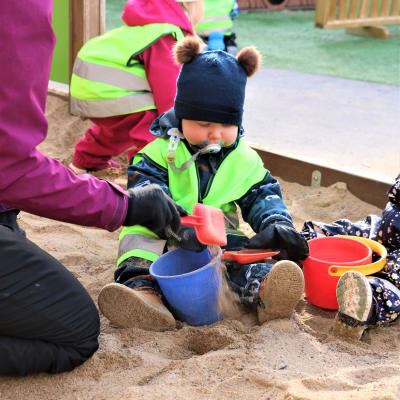 Ett litet barn leker med spade och ämbar i en sandlåda.