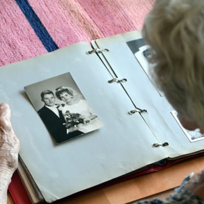 Gammal kvinna ser på ett gammalt bröllopsfoto i ett fotoalbum
