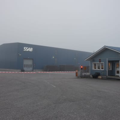 En fabrik i dimmigt septemberväder. Framför byggnaden en röd-vit bom  och ett rött trafikljus.
