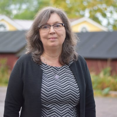 En kvinna står utomhus, ser in i kameran.  Tidig höst.