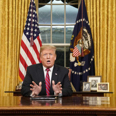 Donald Trump sitter vid ett skrivbord i Ovala rummet och talar.