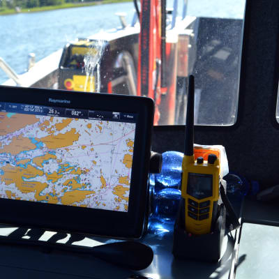 Bilden är tagen från hytten på en båt. Man ser ett digitalt sjökort och en radio framför fönstret.