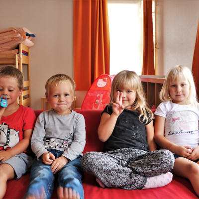 Barnen Kevin, Noel, Saga och Veronica sitter i en röd soffa, tittar in i kameran och ler.